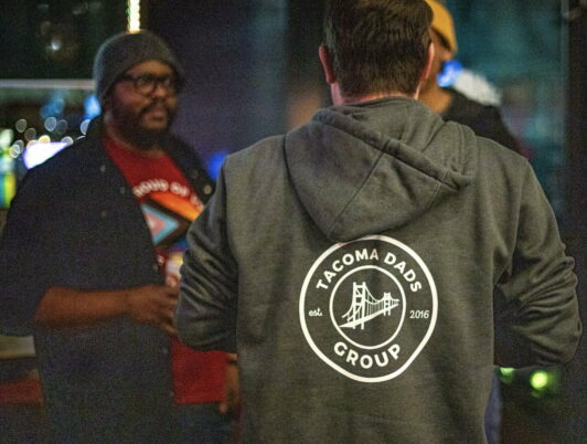 Two people talk together at a meetup of the Tacoma Dads Group in Tacoma Washington. One person wears a hoodie that says 