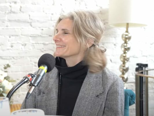Catherine Feeney Tacoma Artist and founder of South Sound Plein Air sits at the podcast mic in a black shirt and grey blazer.