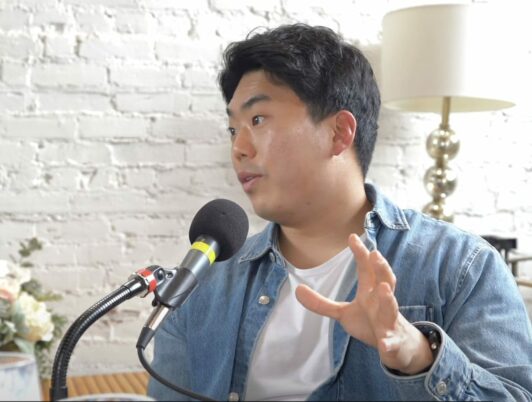 Kevin Lee owner of Third Space Coffee in Tacoma Washington talks into a podcast mic wearing a white tshirt and denim shirt